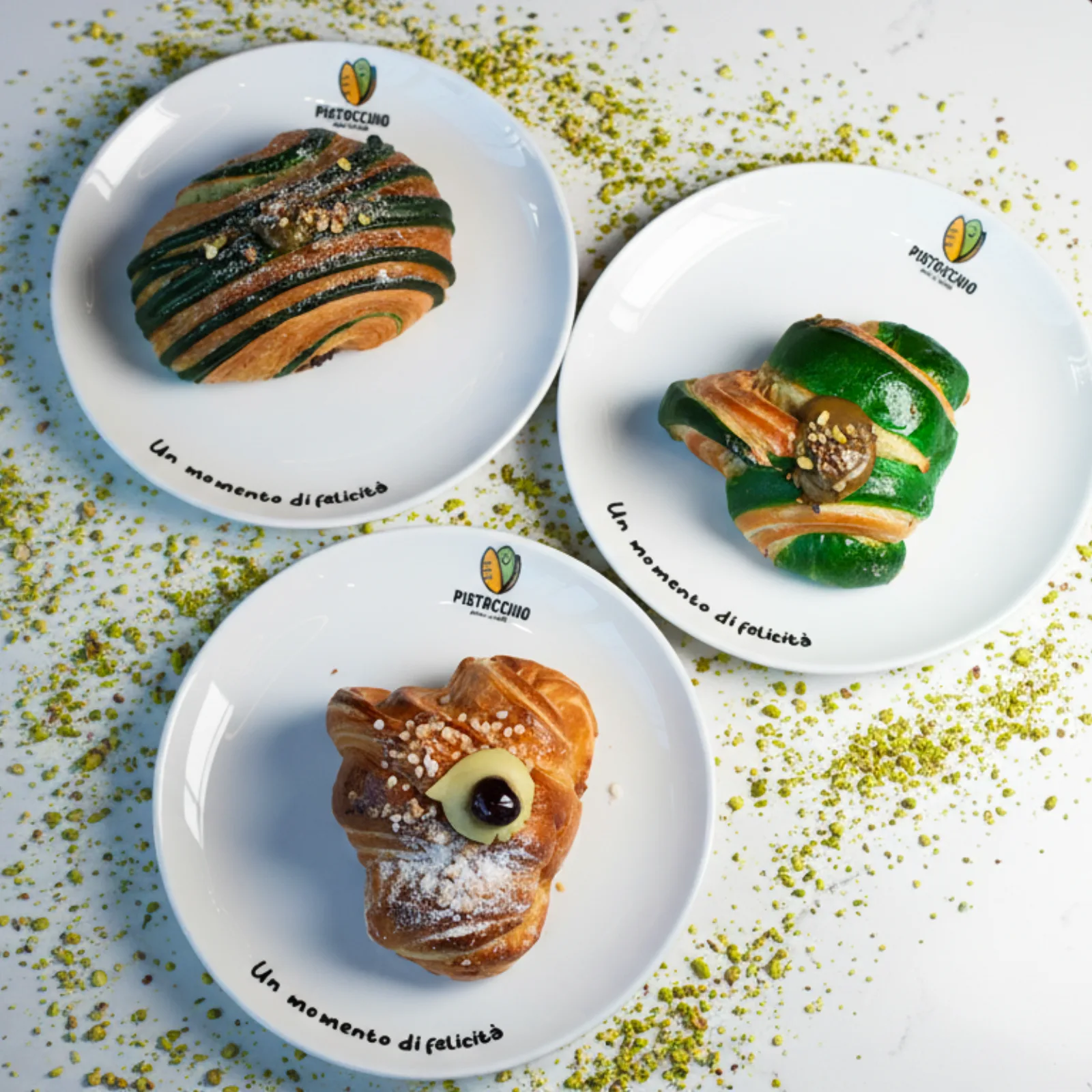 Three filled pastries on branded Pistacchio plates, scattered with chopped pistachio